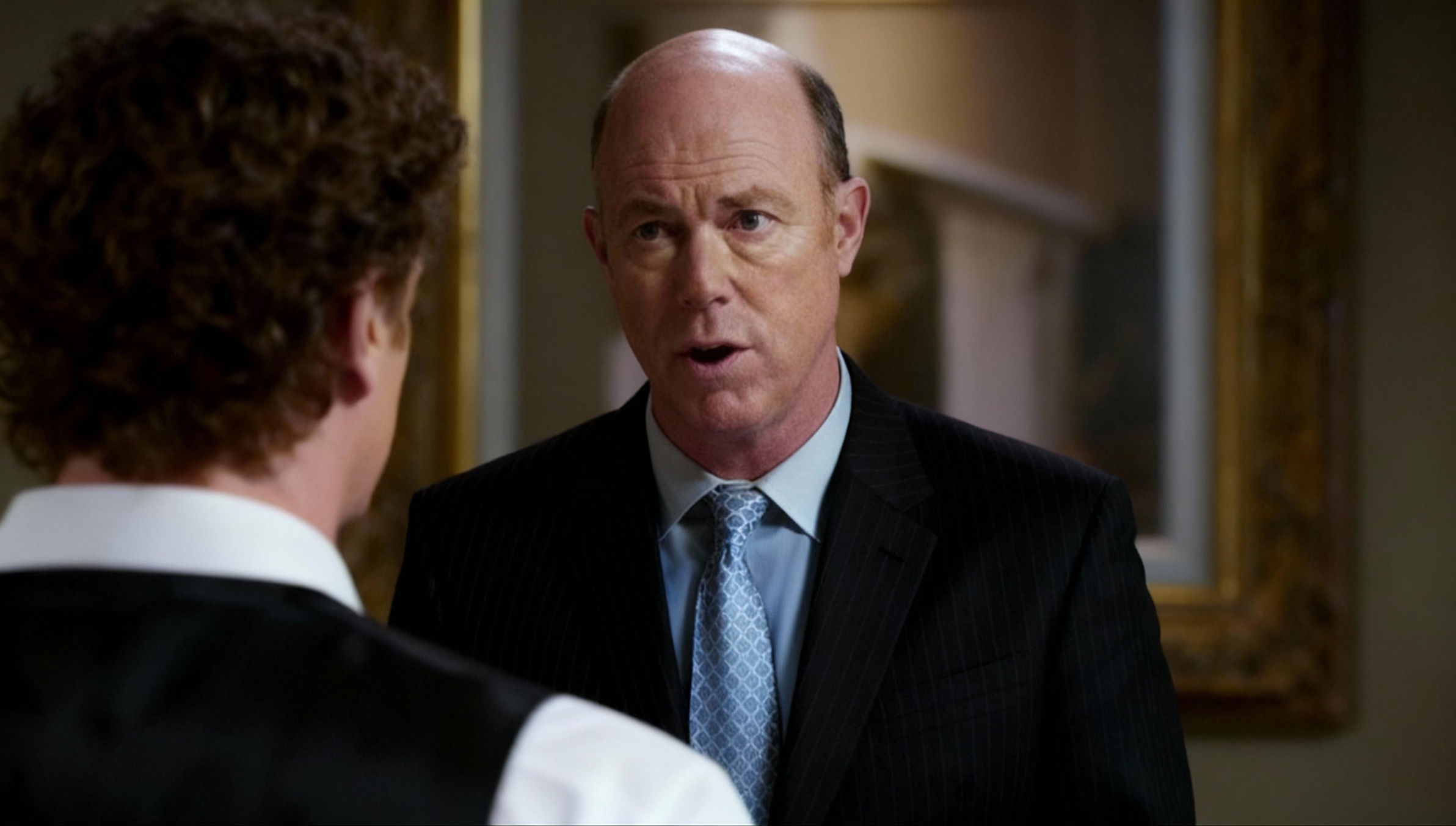 Gale Bertram with a piercing look, monologuing to the man in front of him, proud yet unassuming, imp