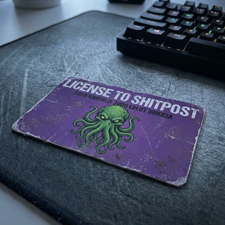 Photorealistic close-up of a worn, purple ID card with the words "LICENSE TO SHITPOST" and other reversed text, resting on a dark gray mousepad. The card features a vibrant image of a Cthulhu-like monster with glowing eyes and tentacles. A portion of a black computer keyboard is visible in the upper right background. Sharp focus on the card, soft bokeh in the background. Natural, diffused lighting creates soft shadows and a slightly moody atmosphere. Subtle scratches and dust on the card surface add to its realism.