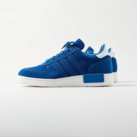 Capture a detailed photograph showcasing Adidas blue suede sneakers with white accents, in a close-up shot. Use a Sony A7R IV camera paired with a FE 50mm f/1.2 GM lens for optimal detail and clarity. The sneakers should be set against a pristine solid white background, utilizing a realistic lighting setup to emphasize contrast and texture. The depth of field should create a soft out-of-focus effect, drawing attention to the intricate details of the suede material. Ensure the image is in ultra-high definition, highlighting every nuance in a raw and natural style without excess stylization. Frame the composition in a 9:16 aspect ratio, capturing the essence of the sneakers in hyper resolution with meticulous attention to detail.
