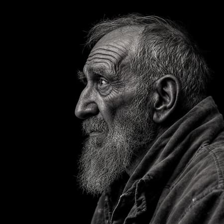 A highly detailed black and white side profile photo of a very tired and old homeless man, captured with a Mamiya camera, set against a deep black background. The man's facial expression is a complex tapestry of wisdom and the trials of time, mingled with a trace of deception, sadness, and madness. His weathered skin and deep-set eyes tell stories of hardship and survival in ultra-high definition.